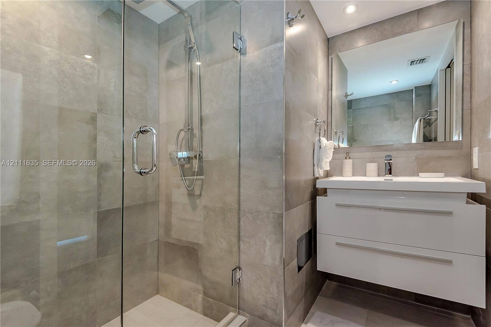 90 Alton Road, #2410, Miami Beach, FL 33139 Walk-in shower with a glass enclosure, wall-mounted floating vanity, large rectangular mirror, and full-height stone-finish tile surround