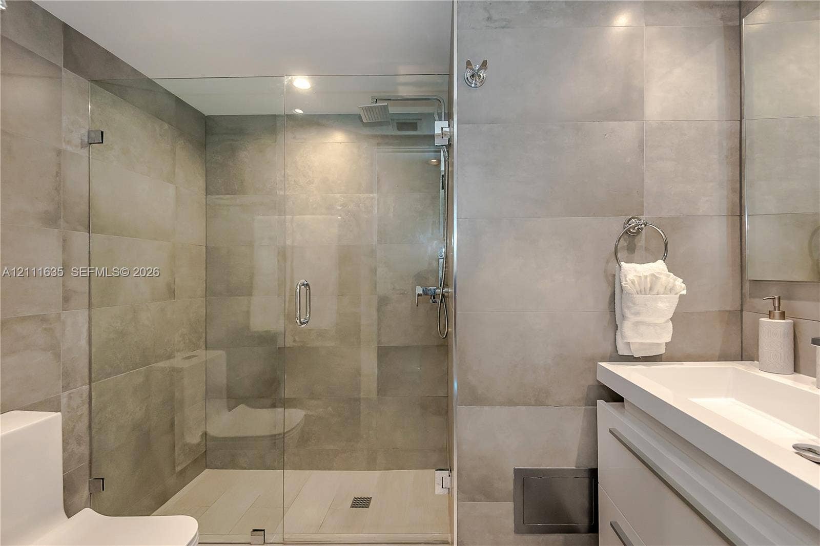 90 Alton Road, #2410, Miami Beach, FL 33139 Walk-in glass-enclosed shower featuring large-format gray wall tiling, rainfall showerhead, floating vanity with integrated rectangular sink, and polished chrome fixtures