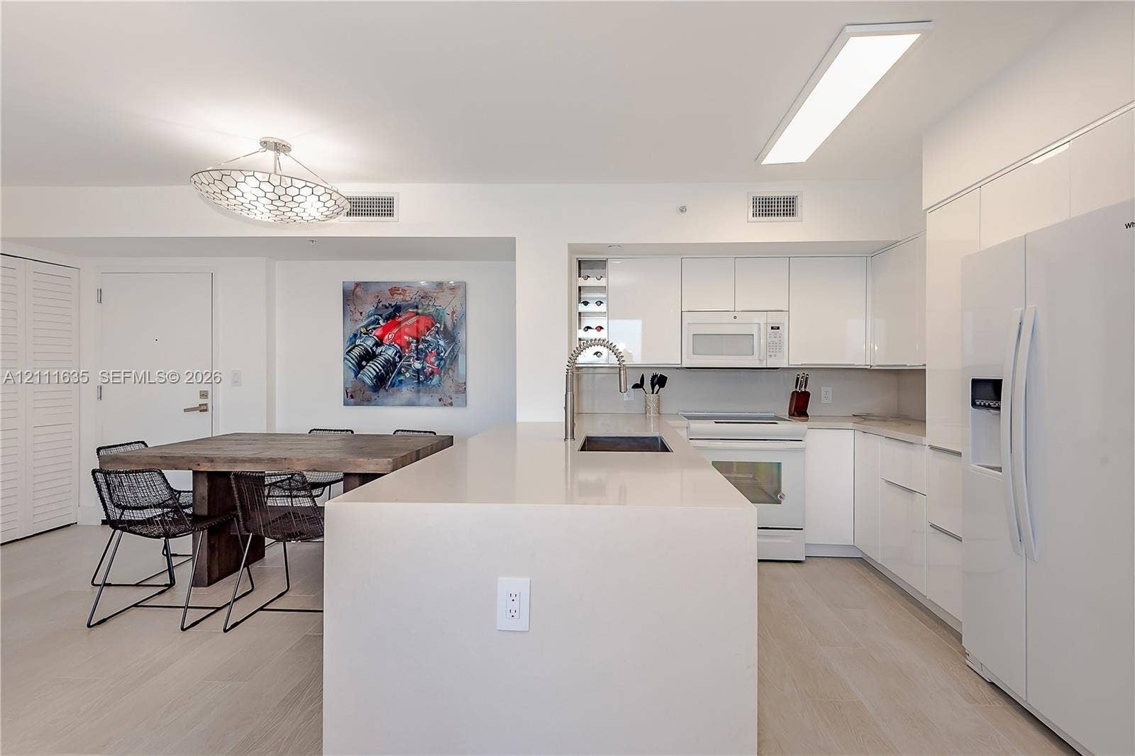 90 Alton Road, #2410, Miami Beach, FL 33139 Kitchen featuring white slab cabinetry, an oversized quartz waterfall island, built-in wine storage, light-toned wood-finish flooring, and a modern geometric pendant light fixture