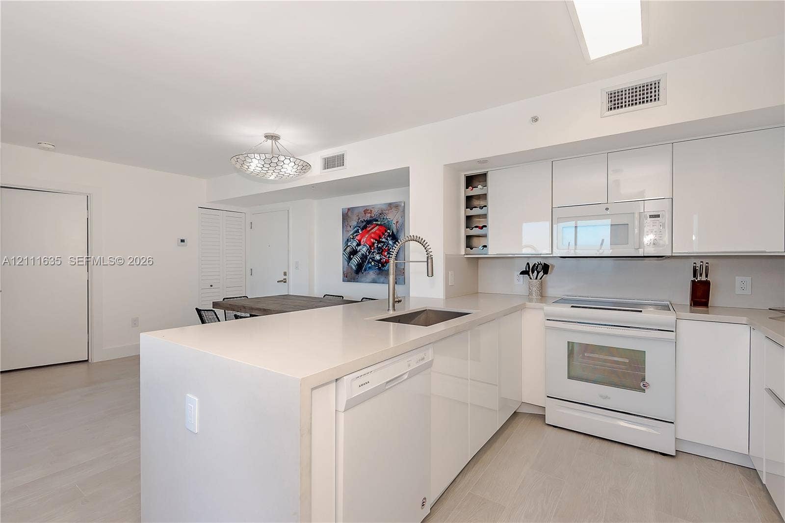 90 Alton Road, #2410, Miami Beach, FL 33139 Kitchen featuring white high-gloss cabinetry, stone-surface countertops, a center island with an undermount sink, built-in wine storage, and light-toned wood-finish flooring