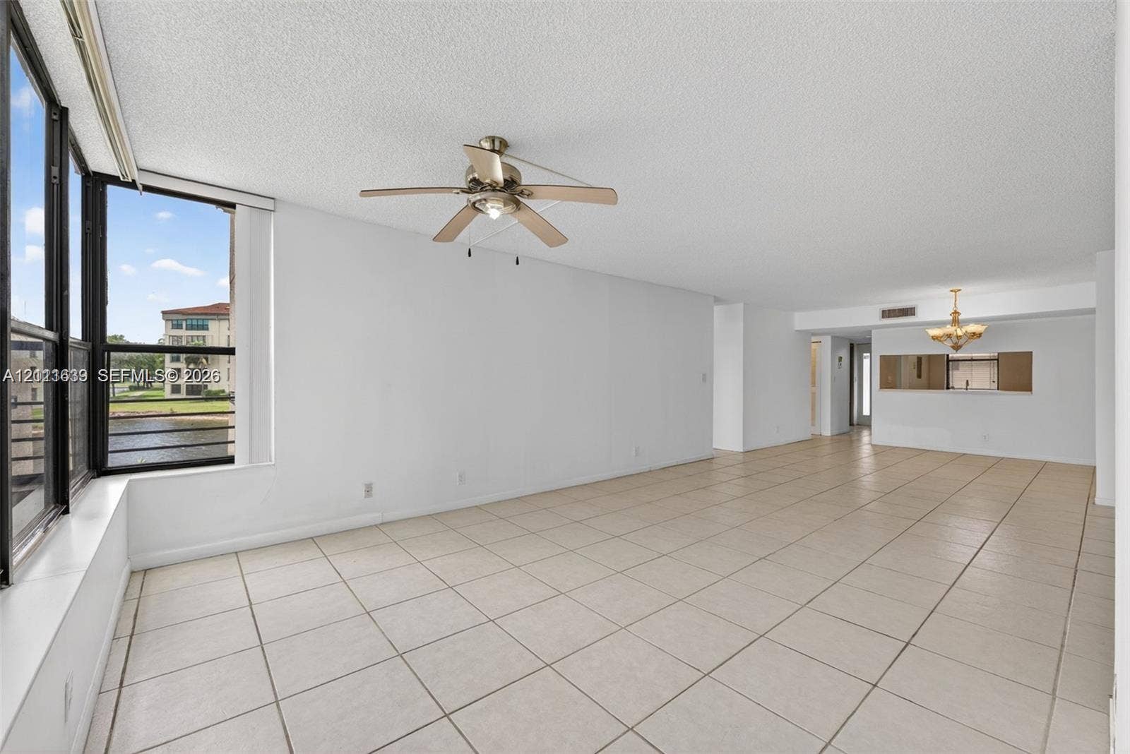 2768 S Carambola Circle S, #206, Coconut Creek, Coconut Creek, FL 33066 Open-concept interior featuring large-format tile flooring, oversized floor-to-ceiling windows, a ceiling fan with integrated lighting, and a decorative chandelier