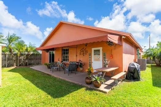 12801 SW 248th Terrace, Homestead, FL 33032 Rear exterior featuring a concrete patio, retractable fabric awning, fenced perimeter, and established landscaping