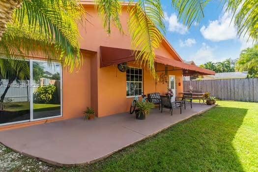 12801 SW 248th Terrace, Homestead, FL 33032 Covered concrete patio with a retractable awning, stucco exterior, sliding glass doors, and a fenced-in backyard