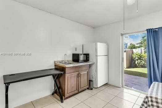 12801 SW 248th Terrace, Homestead, FL 33032 Kitchenette featuring wood-finish cabinetry, stone-texture countertop, inset sink, and tile flooring, with sliding glass door access to an exterior patio