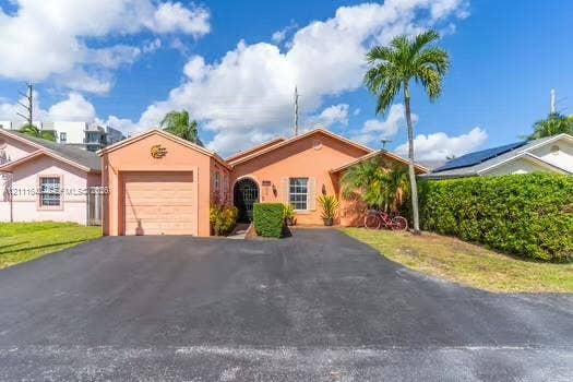 12801 SW 248th Terrace, Homestead, FL 33032 Single-story residence featuring a stucco exterior, attached one-car garage, asphalt driveway, arched entryway with wrought-iron security gate, and manicured shrubbery