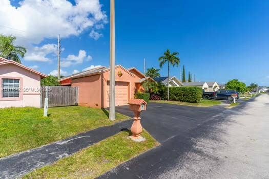 12801 SW 248th Terrace, Homestead, FL 33032 Single-story stucco exterior featuring a built-in garage, asphalt driveway, and ornamental pedestal mailbox