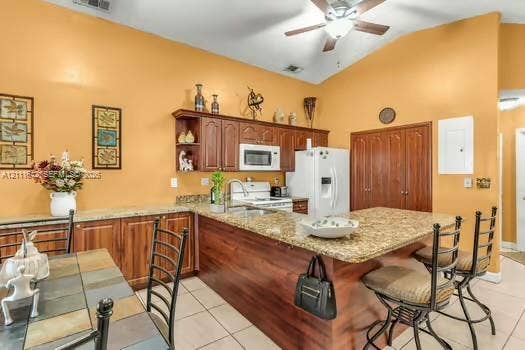 12801 SW 248th Terrace, Homestead, FL 33032 Kitchen featuring stone countertops, wood-finish cabinetry, an extended breakfast bar, tile flooring, and a vaulted ceiling with a mounted light-and-fan fixture