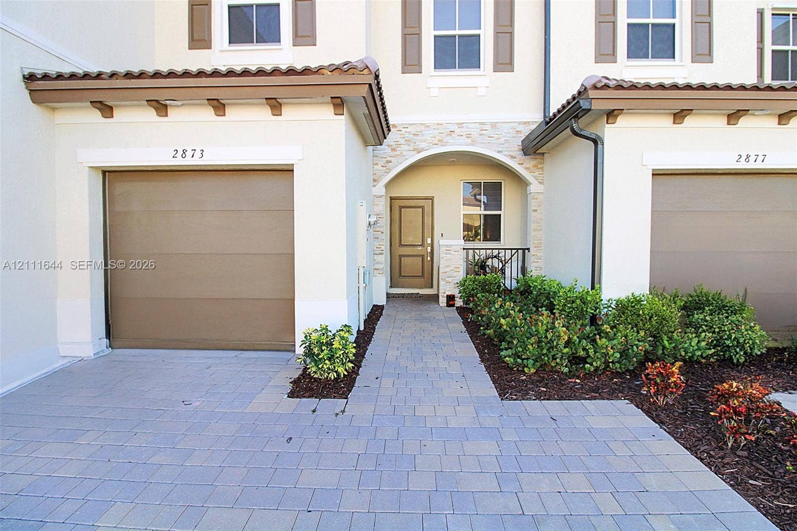 2873 SE 24th Avenue, Homestead, FL 33035 Exterior featuring a paver driveway, single-car garage, stone veneer entryway accents, and a covered portico with arched detailing