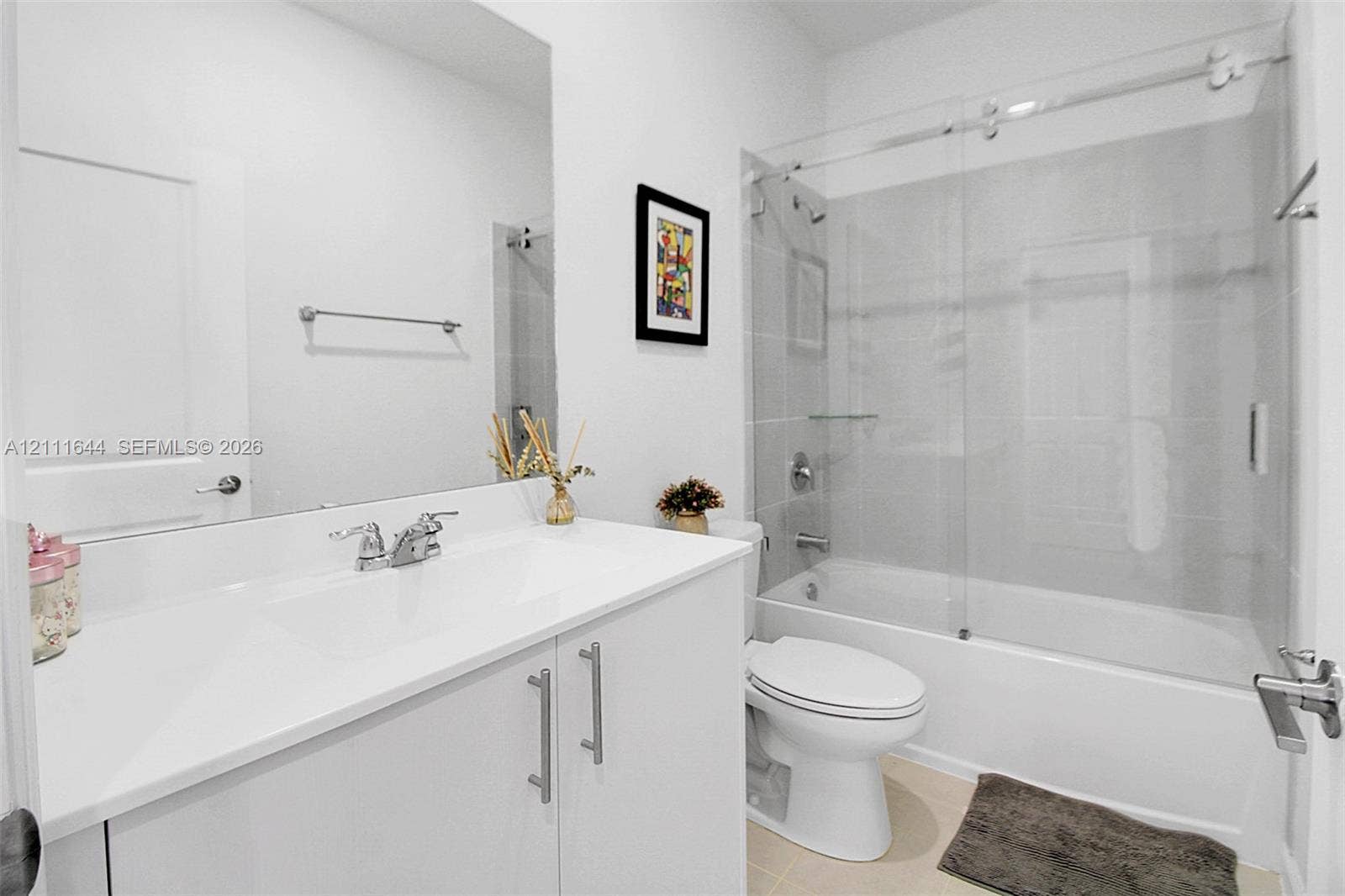 2873 SE 24th Avenue, Homestead, FL 33035 Bathroom featuring a white vanity with a composite countertop, an expansive frameless mirror, and a tub-shower combination enclosed by a sliding glass door with polished chrome hardware
