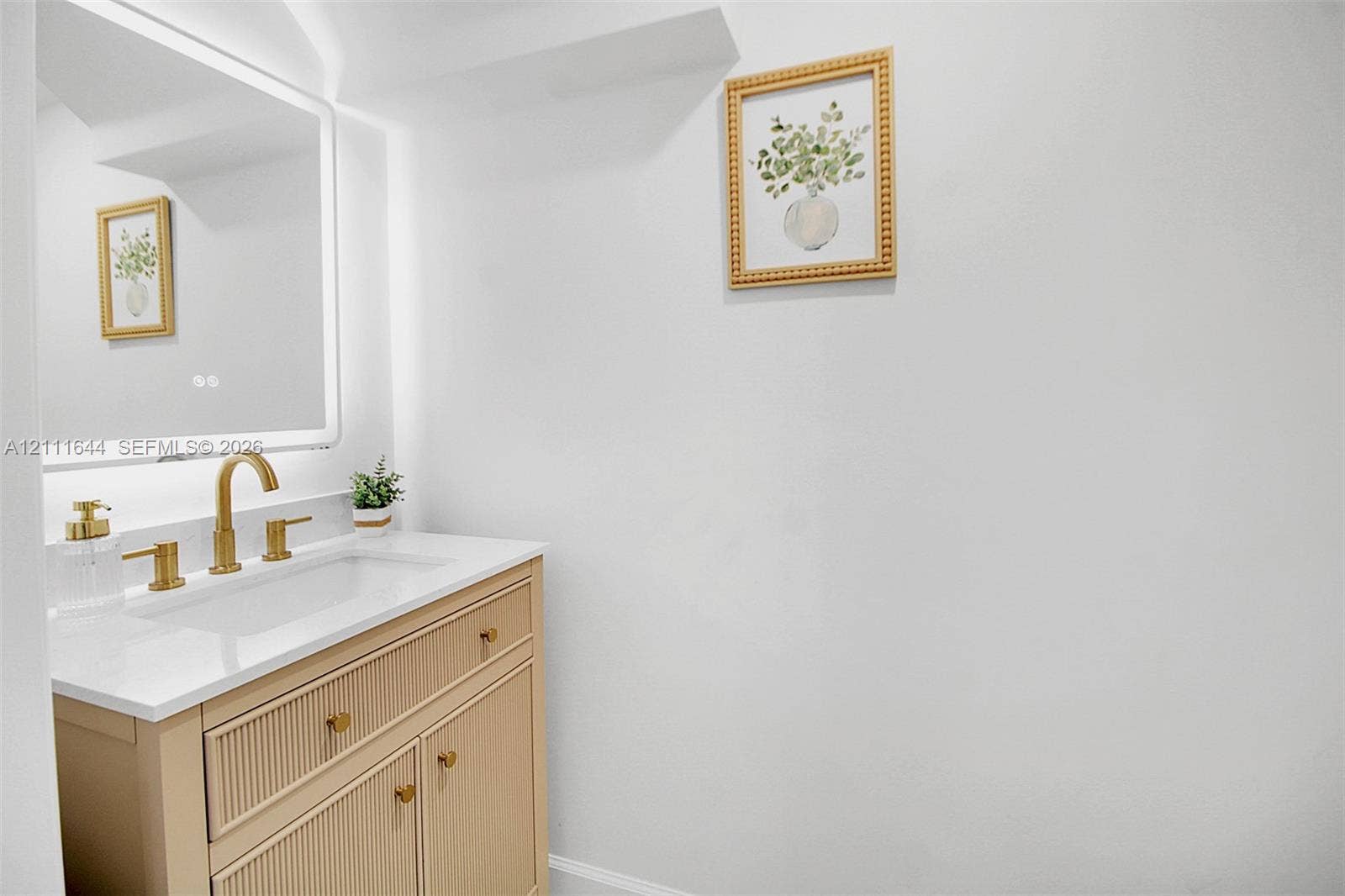 2873 SE 24th Avenue, Homestead, FL 33035 Fluted wood-finish vanity with a stone countertop, integrated rectangular sink, brass-toned faucet, and an LED-backlit mirror