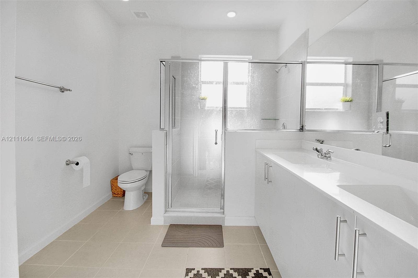 2873 SE 24th Avenue, Homestead, FL 33035 Dual-sink vanity with white cabinetry and solid surface countertop, glass-enclosed shower, polished chrome fixtures, and neutral floor tiling