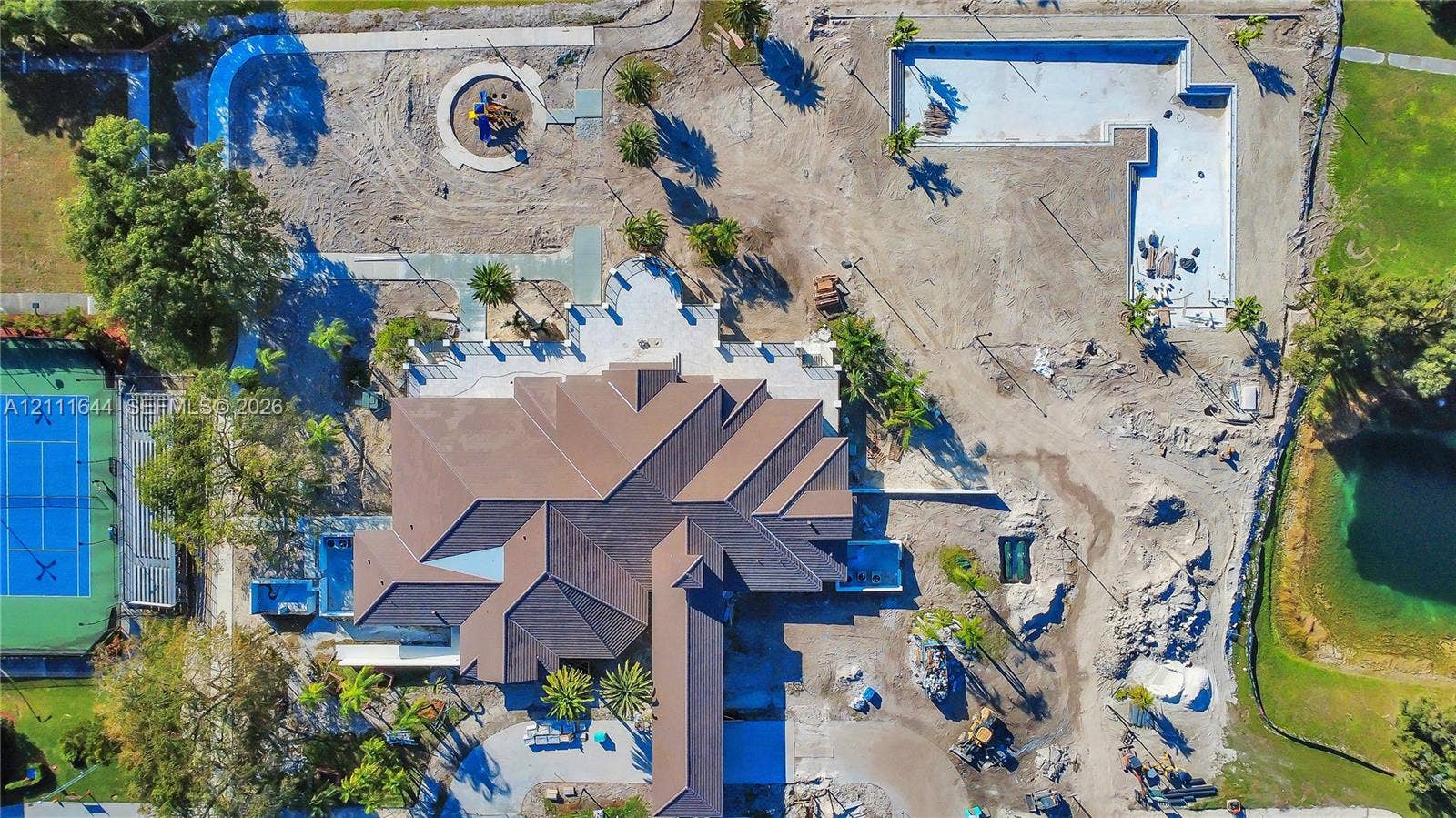 2873 SE 24th Avenue, Homestead, FL 33035 Aerial view of a sprawling property featuring a multi-gabled roofline, a dedicated tennis court, a large pool structure, and surrounding grounds