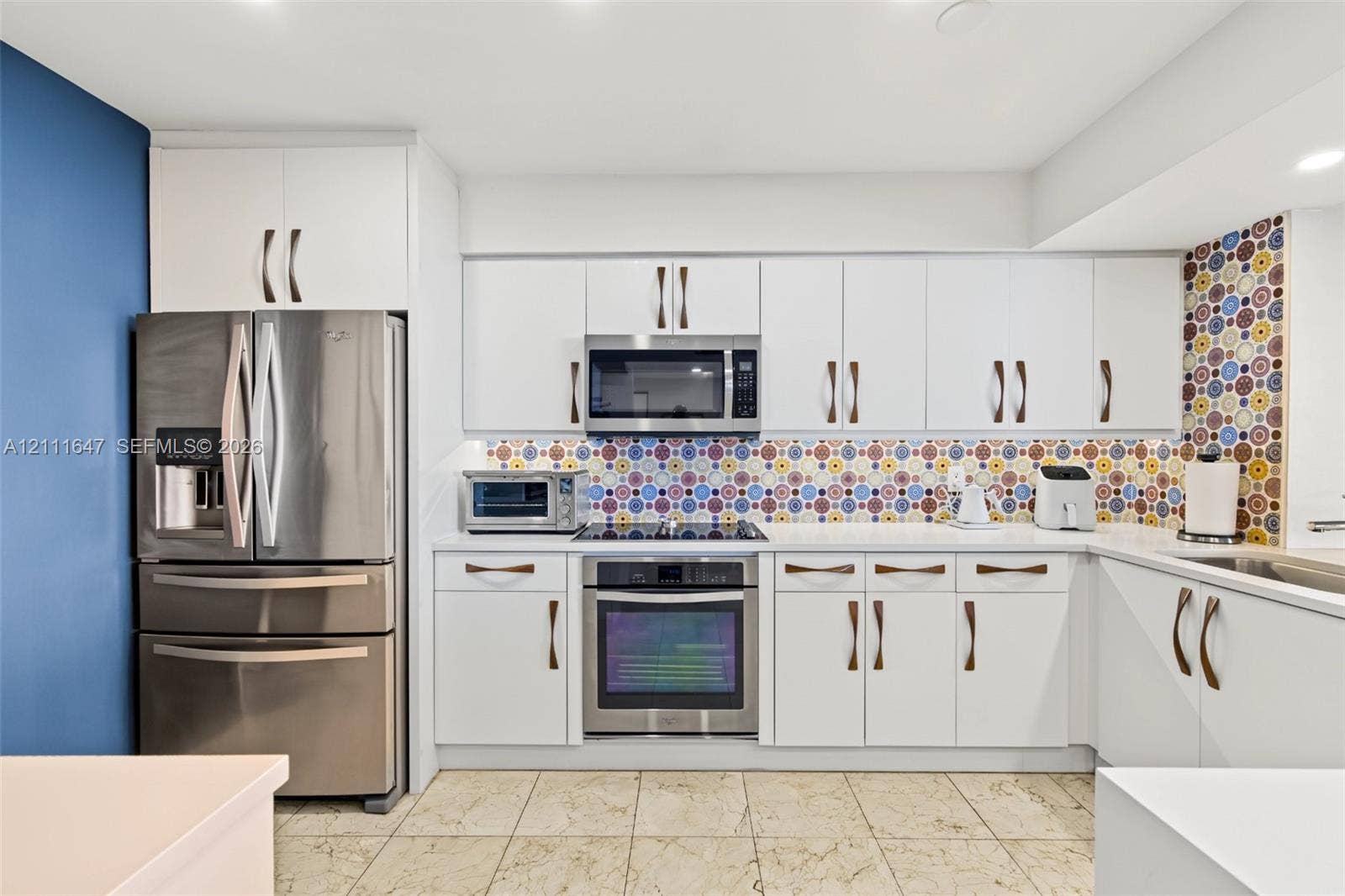 8925 Collins Avenue, #4J, Surfside, FL 33154 Kitchen featuring white cabinetry, stainless steel appliances, patterned tile backsplash, and stone-finish tile flooring