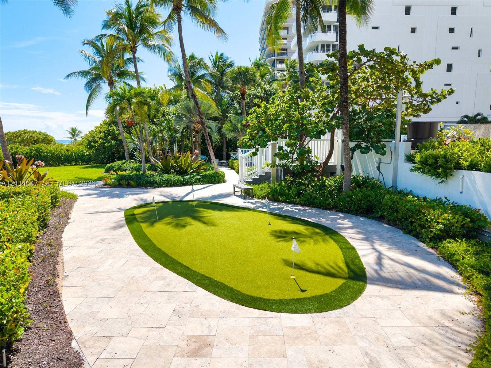 8925 Collins Avenue, #4J, Surfside, FL 33154 Putting green with synthetic turf surrounded by natural stone paver hardscaping, mature palm trees, and landscaped gardens