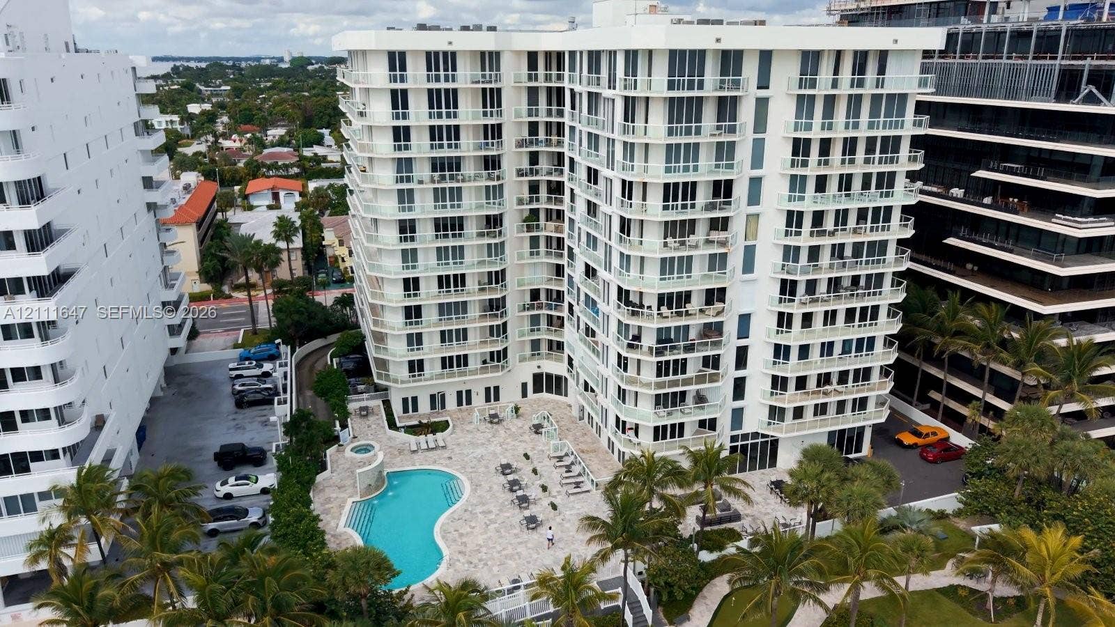 8925 Collins Avenue, #4J, Surfside, FL 33154 High-rise residential building featuring private balconies, an outdoor swimming pool, stone-paved patio, and mature palm trees