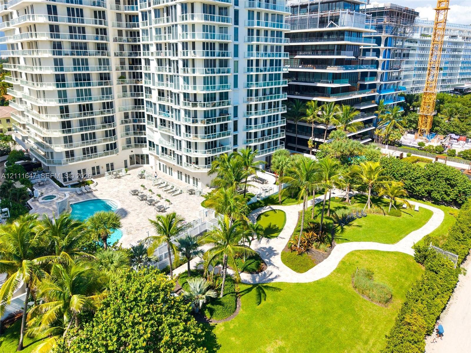 8925 Collins Avenue, #4J, Surfside, FL 33154 High-rise residential exterior featuring expansive paved pool deck, custom-shaped swimming pool, integrated spa, and manicured landscaping with mature palm trees