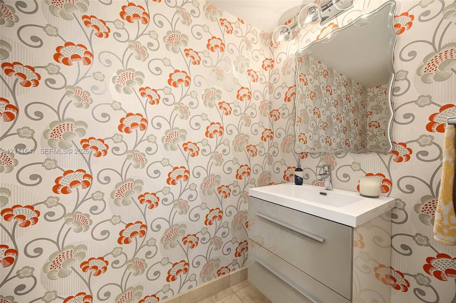 8925 Collins Avenue, #4J, Surfside, FL 33154 Wall-mounted vanity with a rectangular sink, patterned wallpaper, and a decorative-edge mirror with integrated three-bulb light fixture