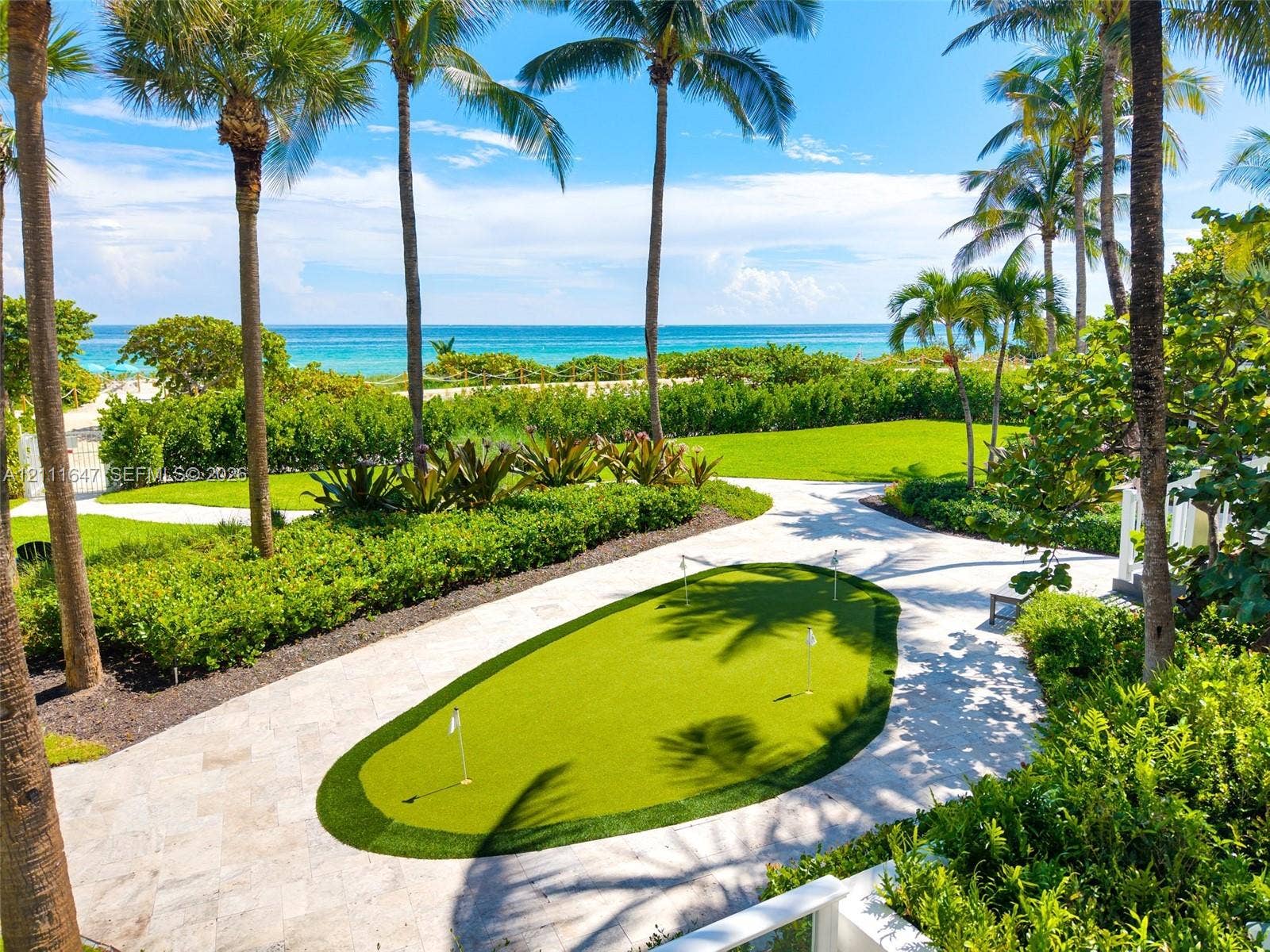 8925 Collins Avenue, #4J, Surfside, FL 33154 Putting green with synthetic turf, stone-paved patio, manicured lawn, and mature palm trees