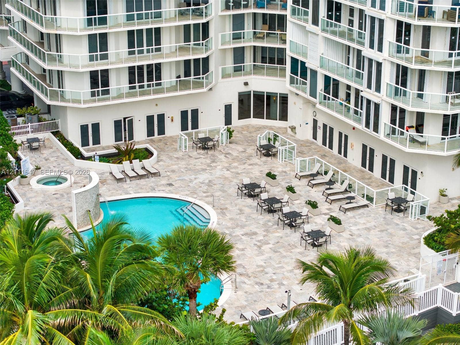 8925 Collins Avenue, #4J, Surfside, FL 33154 Outdoor common area featuring a swimming pool, integrated spa, waterfall feature, and stone-finish decking surrounded by palm trees