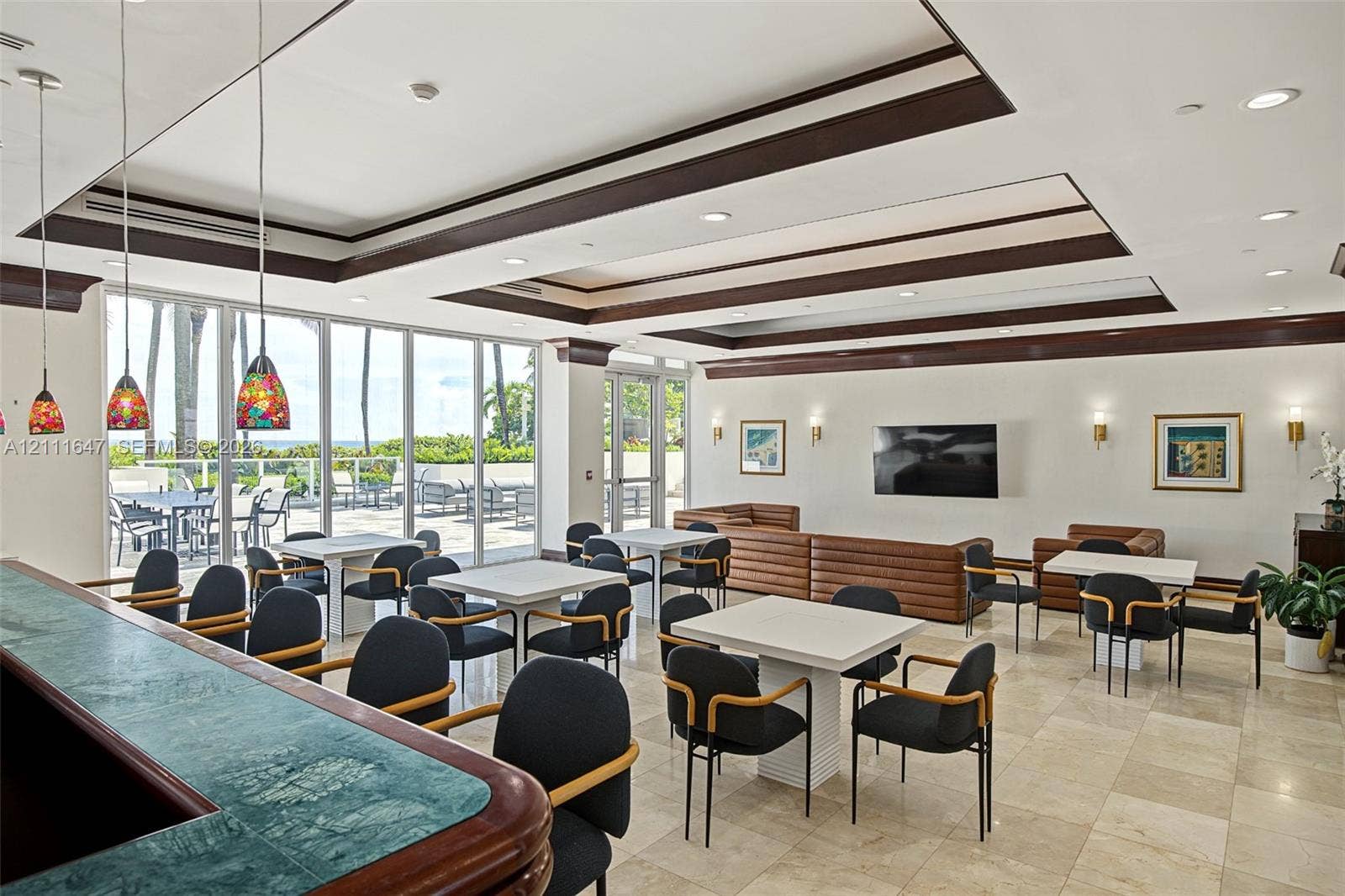 8925 Collins Avenue, #4J, Surfside, FL 33154 Spacious common area featuring recessed tray ceilings with dark wood trim, tile flooring, built-in stone-top bar, and expansive floor-to-ceiling glass wall panels