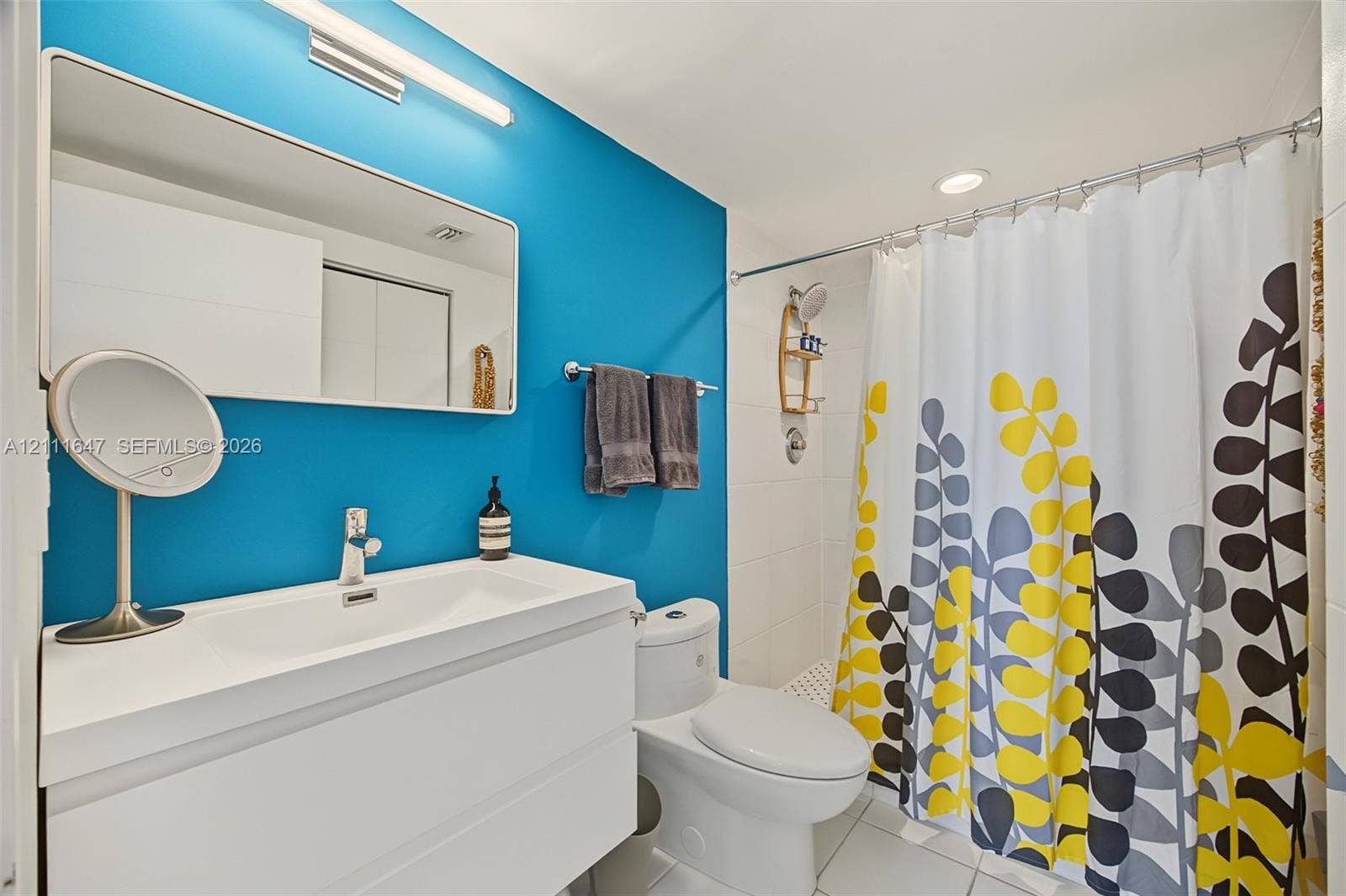8925 Collins Avenue, #4J, Surfside, FL 33154 Wall-mounted rectangular mirror, white floating vanity with integrated sink, polished chrome single-handle faucet, and tiled shower surround