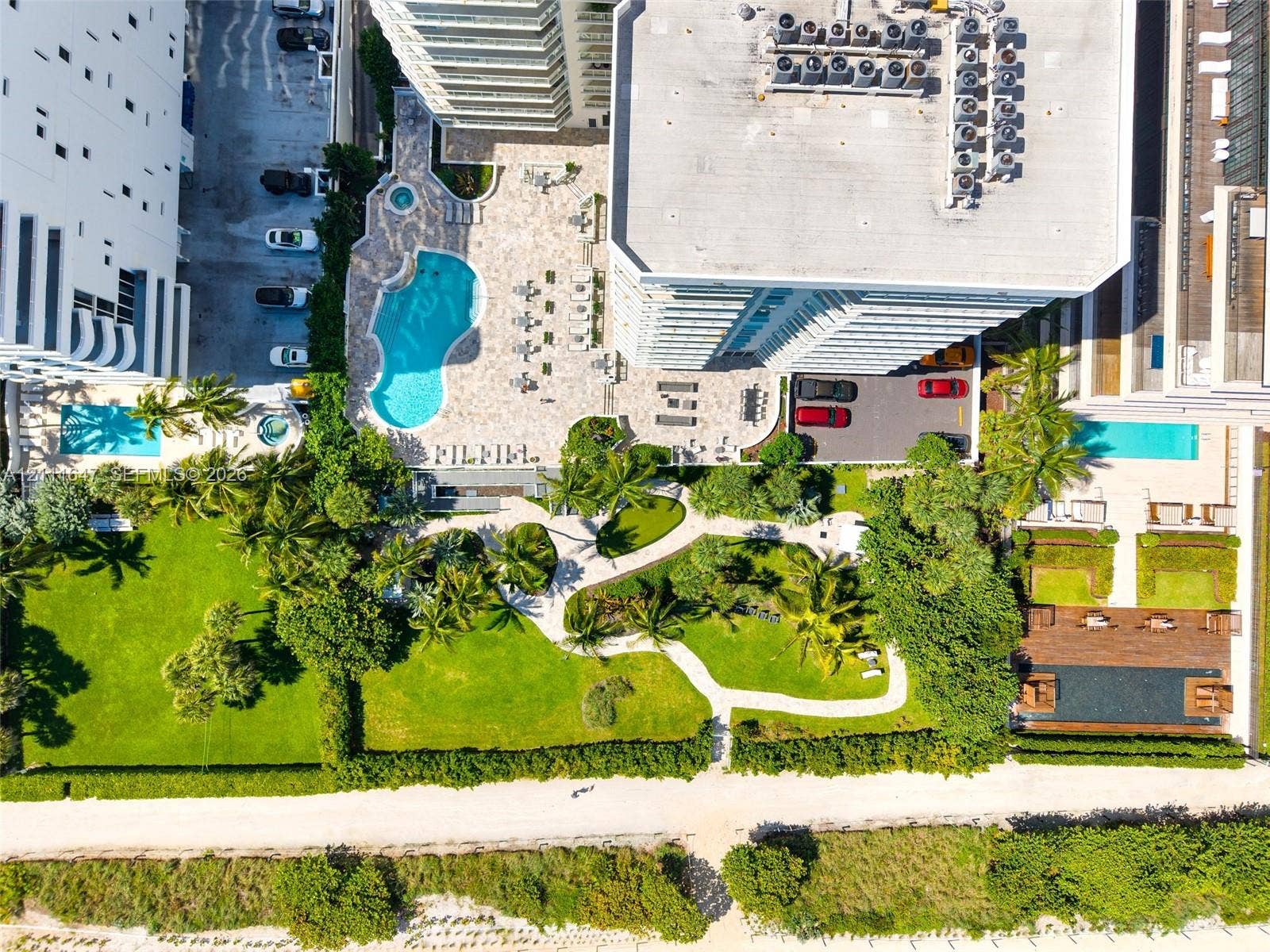 8925 Collins Avenue, #4J, Surfside, FL 33154 Aerial perspective featuring a swimming pool, integrated spa, expansive landscaped green space with manicured lawn, stone-paved patio, and established palm trees