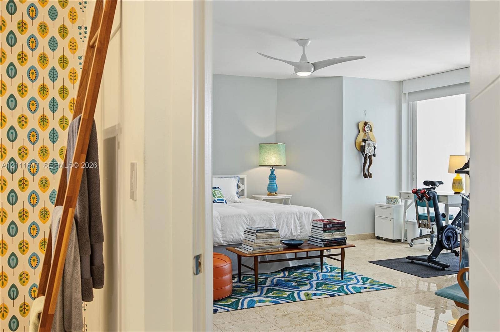8925 Collins Avenue, #4J, Surfside, FL 33154 Polished stone flooring, floor-to-ceiling windows, white-finish ceiling fan with integrated lighting, and accent wall featuring a patterned leaf motif