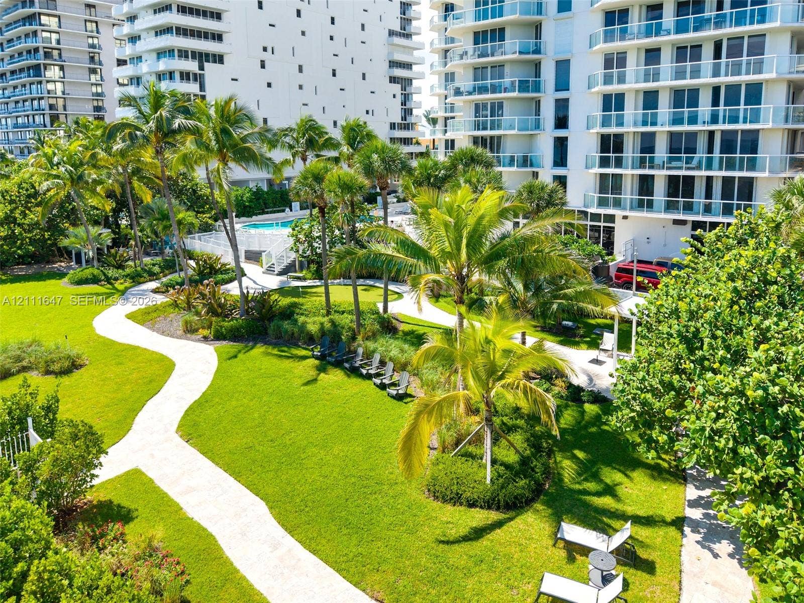 8925 Collins Avenue, #4J, Surfside, FL 33154 Expansive landscaped grounds featuring winding paved pathways, mature palm trees, manicured lawns, and a swimming pool
