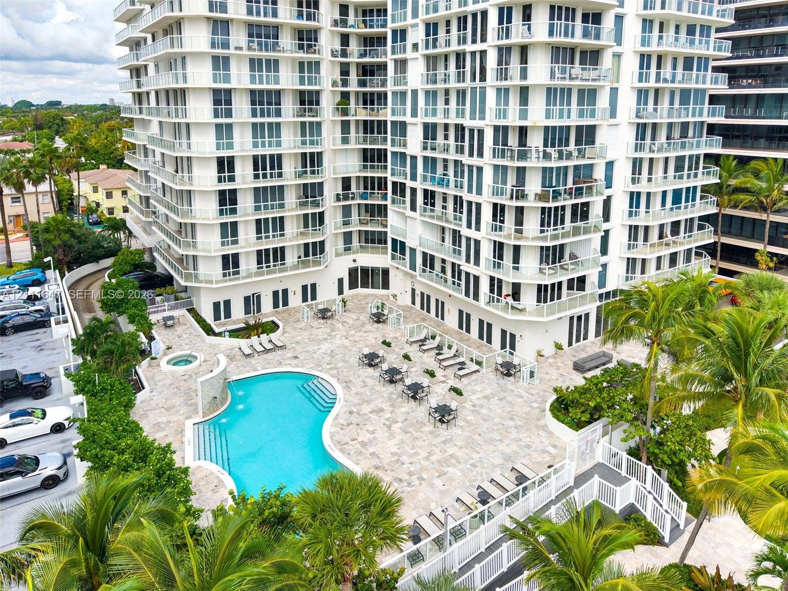 8925 Collins Avenue, #4J, Surfside, FL 33154 High-rise residential exterior featuring a free-form swimming pool, integrated spa, stone-paver pool deck, and glass-paneled balconies