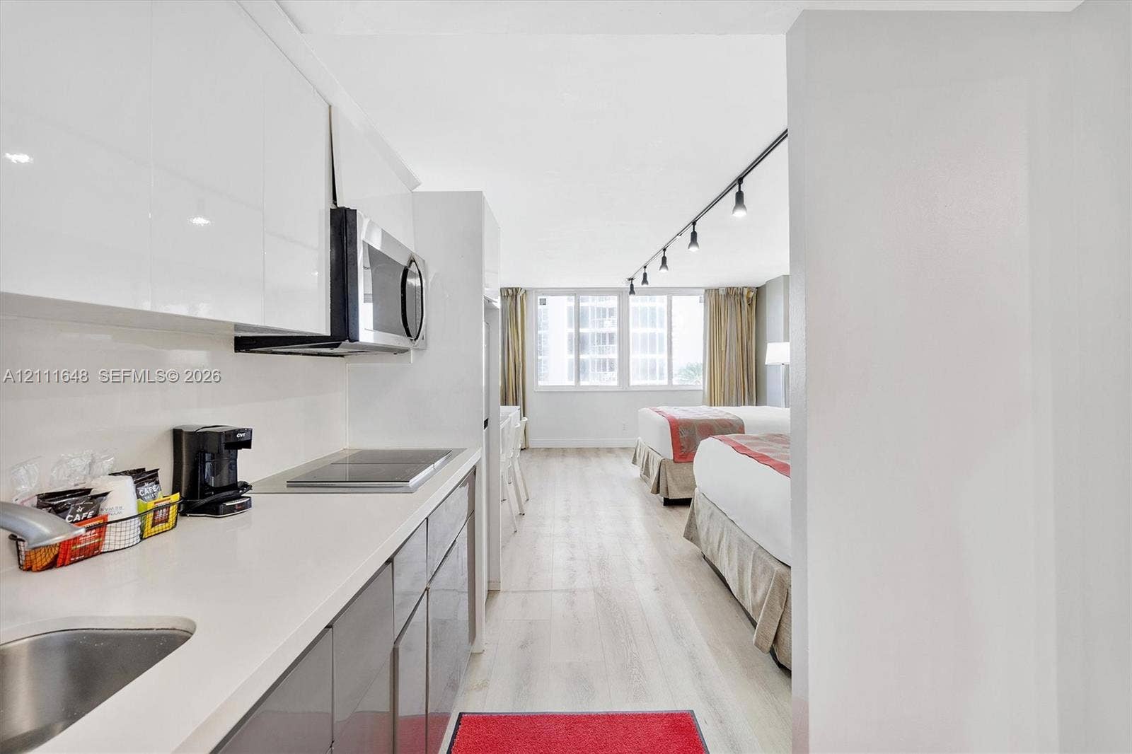 19201 Collins Avenue, #518, Sunny Isles Beach, FL 33160 Kitchen featuring high-gloss cabinetry, stone-finish countertops, integrated microwave, and built-in cooktop, complemented by wood-finish flooring and modern track lighting