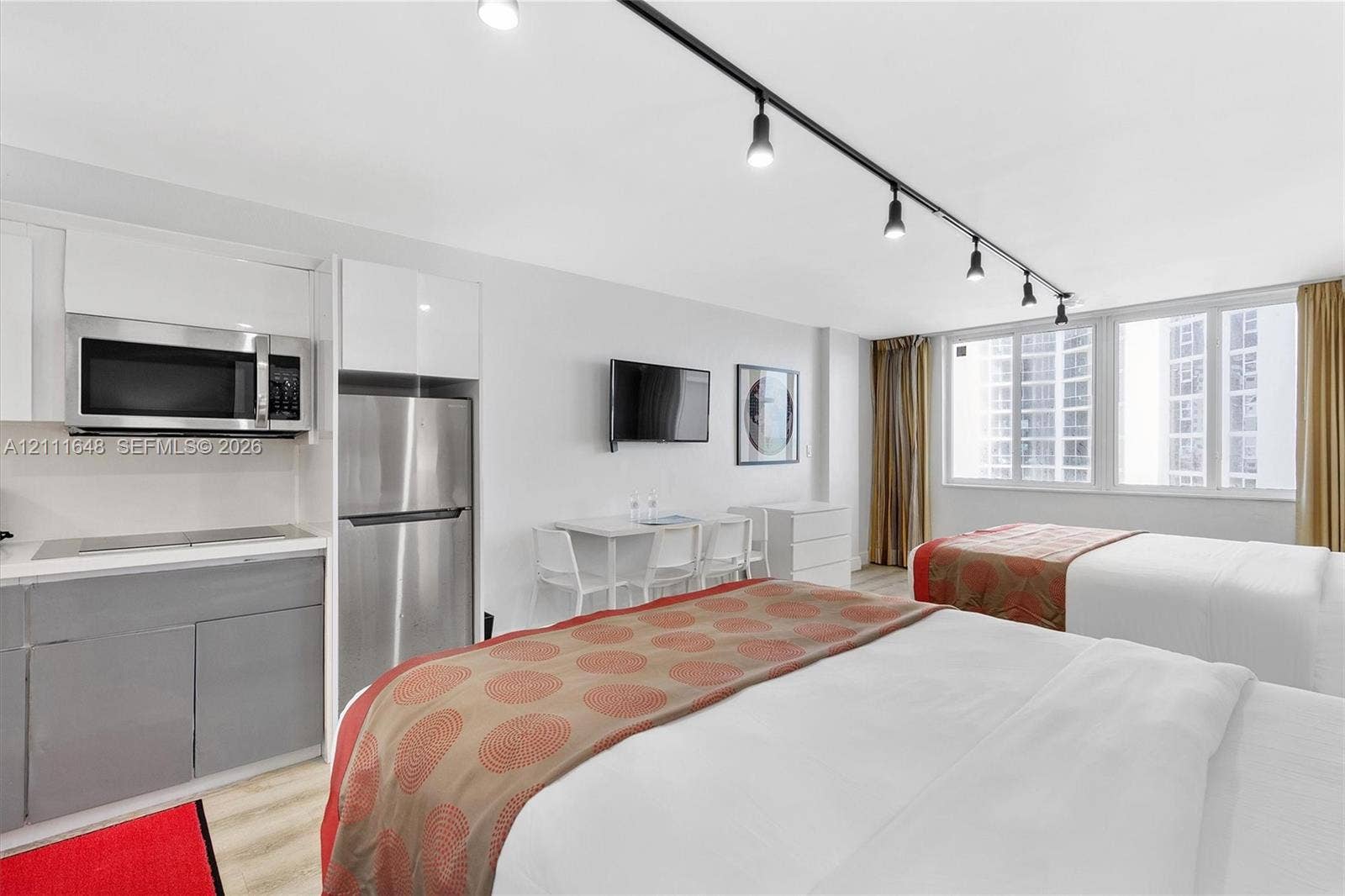 19201 Collins Avenue, #518, Sunny Isles Beach, FL 33160 Kitchenette featuring glossy white upper cabinetry, stainless steel microwave, stainless steel refrigerator, and matte grey lower cabinetry, complemented by track lighting and wood-finish flooring