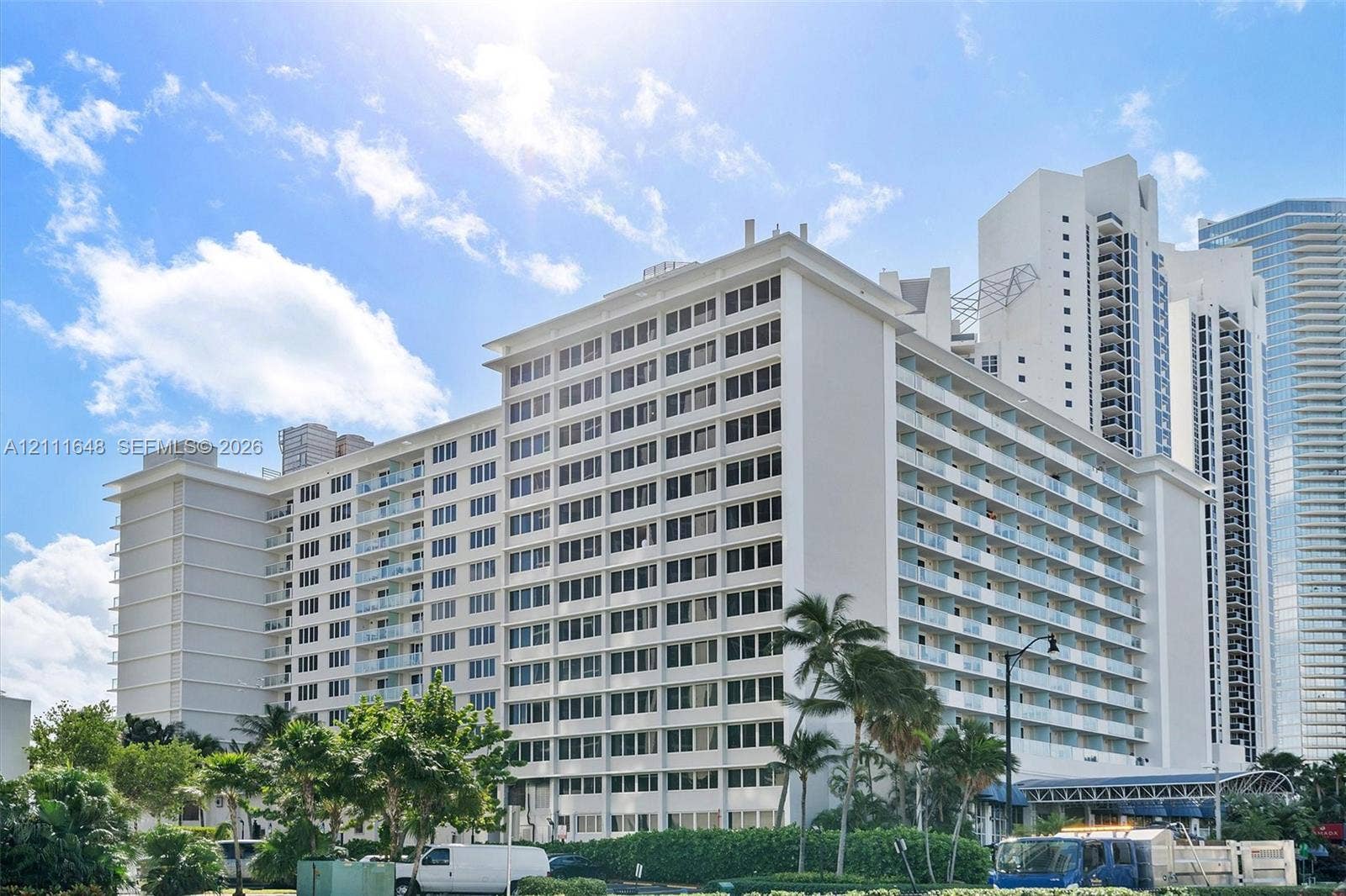 19201 Collins Avenue, #518, Sunny Isles Beach, FL 33160 High-rise multi-story exterior featuring white stucco facade, expansive glass-railed balconies, and mature landscaping