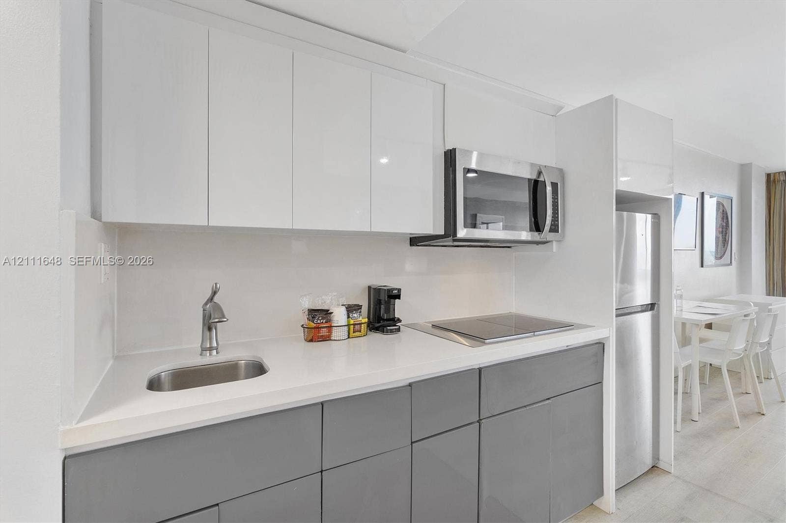 19201 Collins Avenue, #518, Sunny Isles Beach, FL 33160 Kitchenette featuring flat-panel white upper cabinets, grey lower cabinetry, stainless steel appliances, solid surface countertops, and an integrated basin sink
