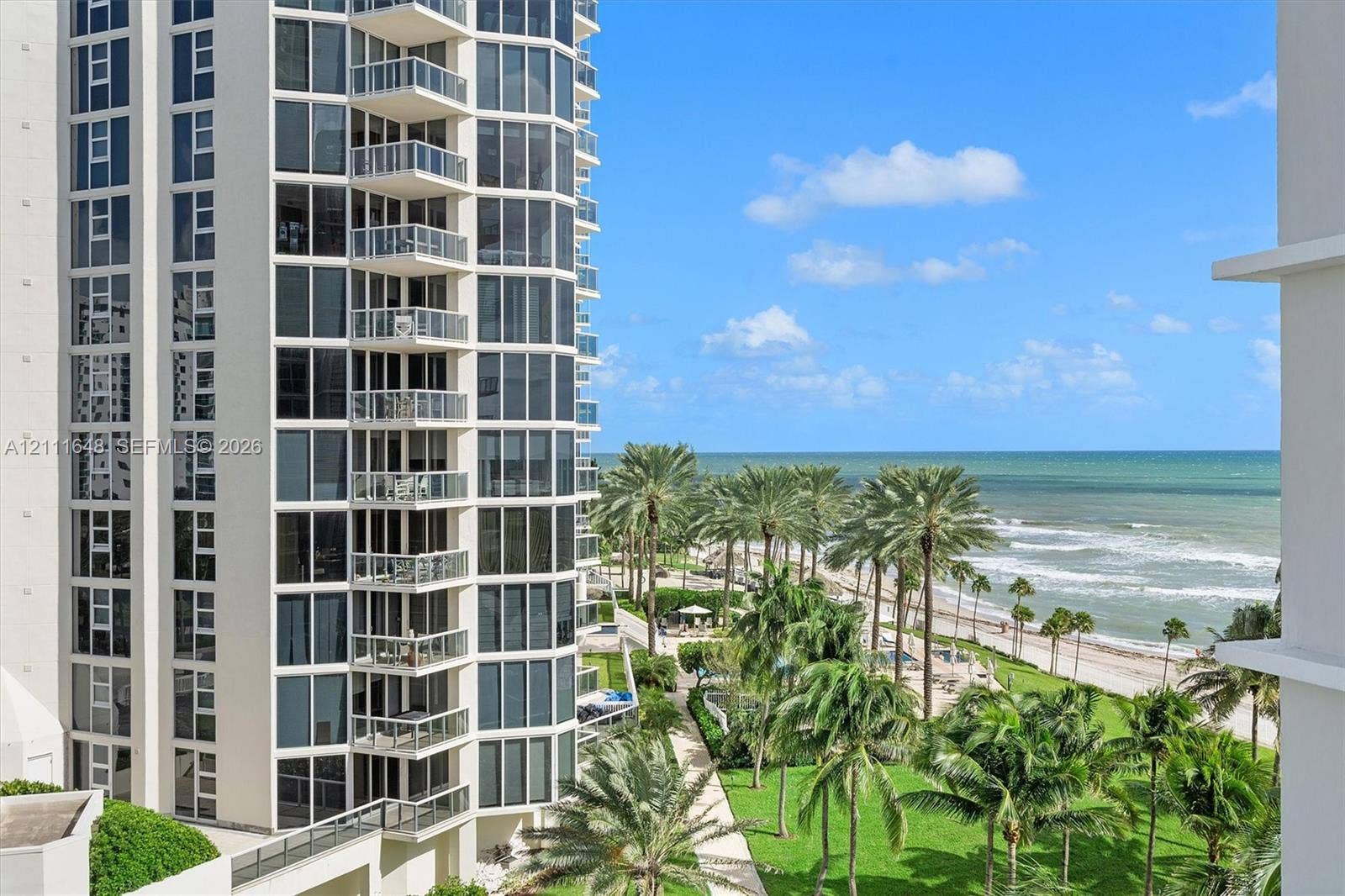 19201 Collins Avenue, #518, Sunny Isles Beach, FL 33160 High-rise tower featuring floor-to-ceiling glass windows and stacked private balconies, set against an oceanfront backdrop with palm-lined landscaping