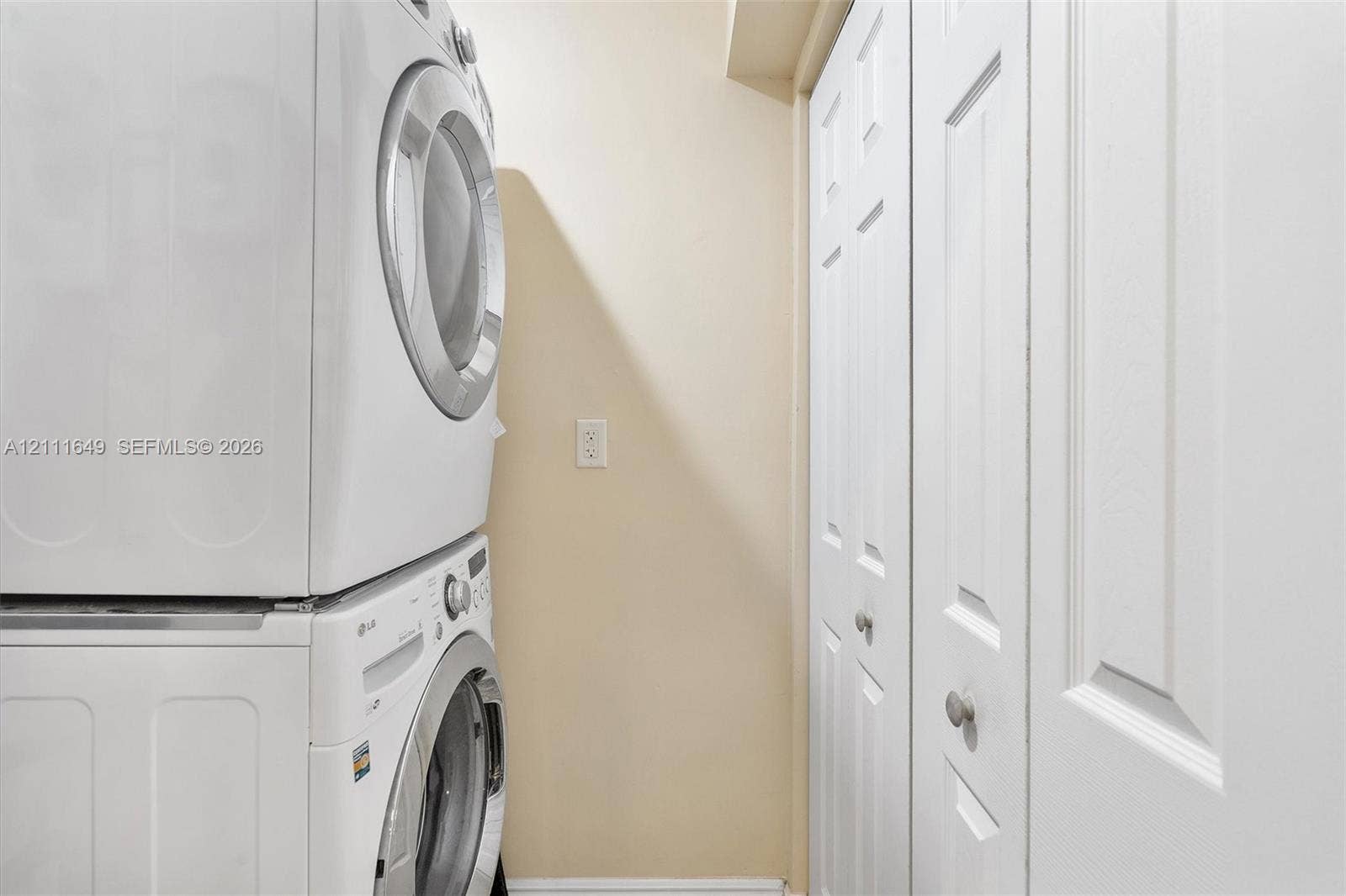 Stacked laundry unit with white finish and bifold closet doors