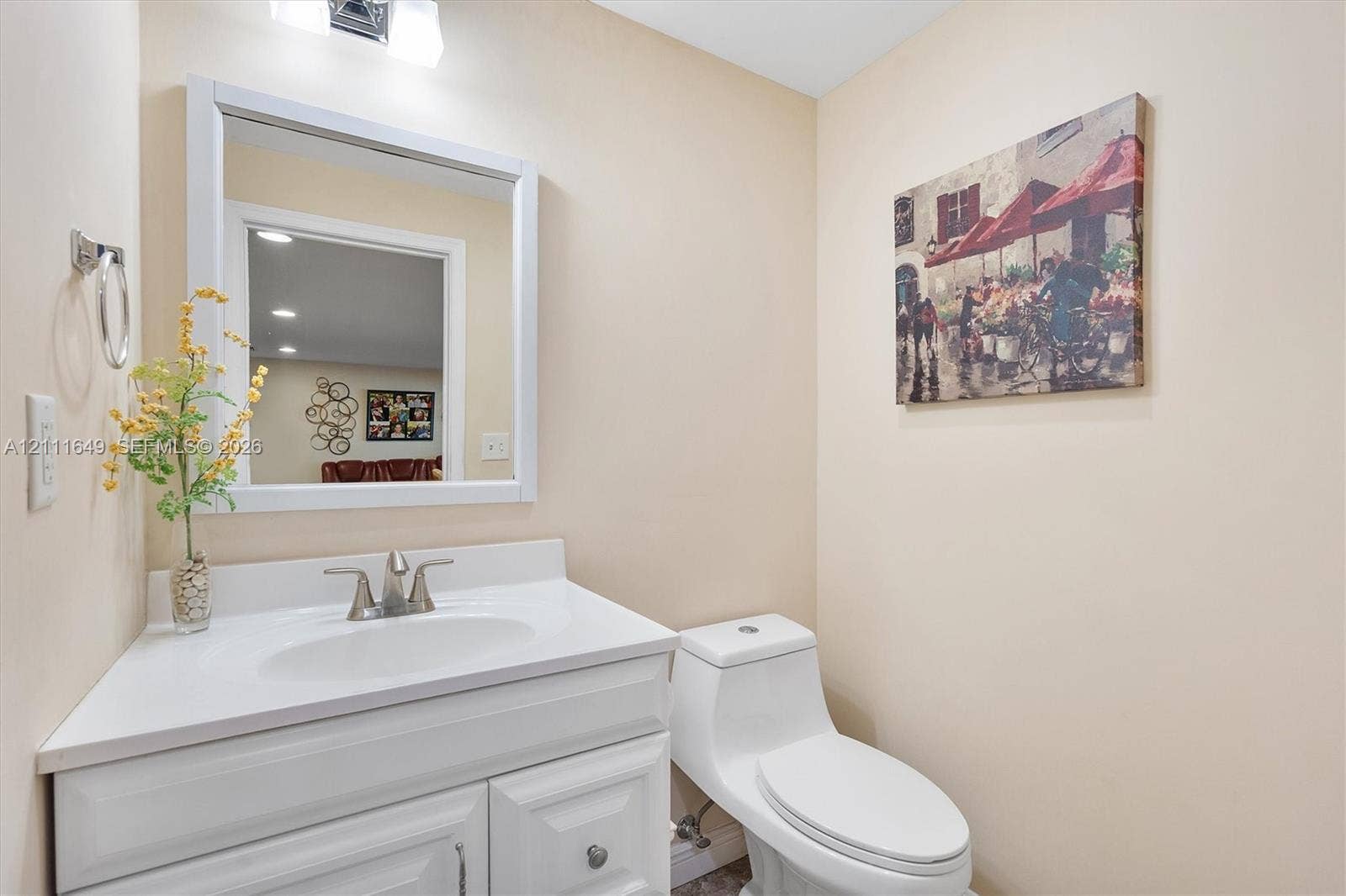White vanity cabinet with an integrated sink, solid-surface countertop, metal faucet, framed wall mirror, and dual-flush toilet