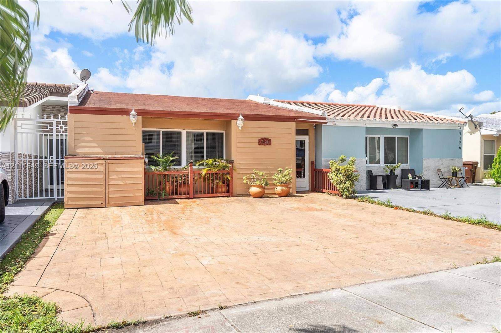 Single-story exterior featuring a paver driveway, horizontal siding, tile roof, and enclosed entryway with metal gate