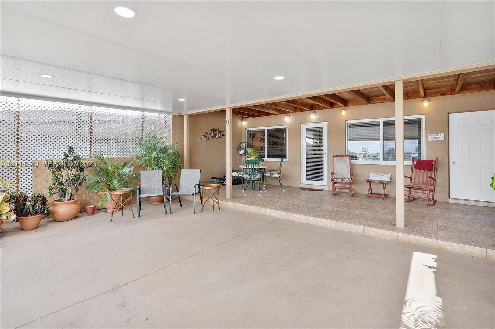 Covered outdoor patio featuring a concrete floor, recessed lighting, exposed wood ceiling beams, and white lattice privacy screening