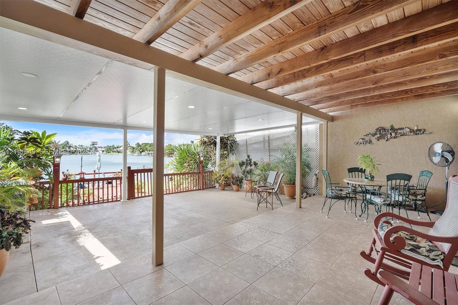 Covered patio featuring a tile floor, exposed wood beam ceiling, recessed lighting, and a railed wood deck overlooking the water