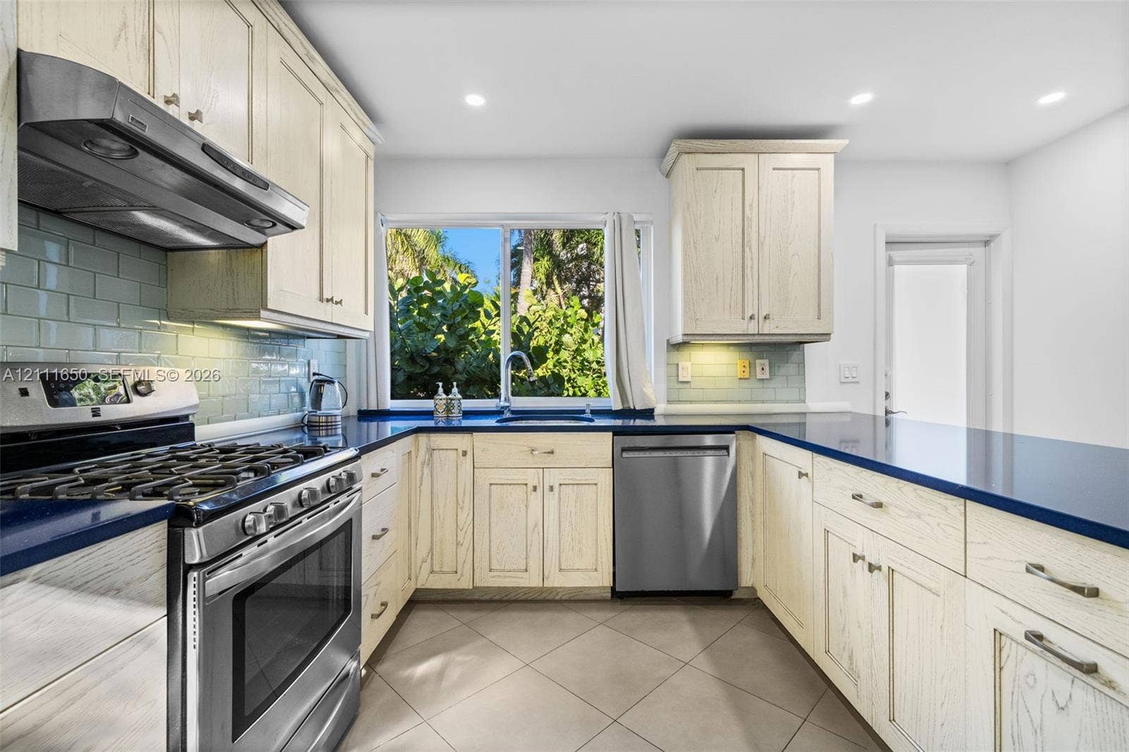 Kitchen featuring light-toned wood cabinetry, dark solid-surface countertops, stainless steel appliances, a tile backsplash, and ceramic tile flooring