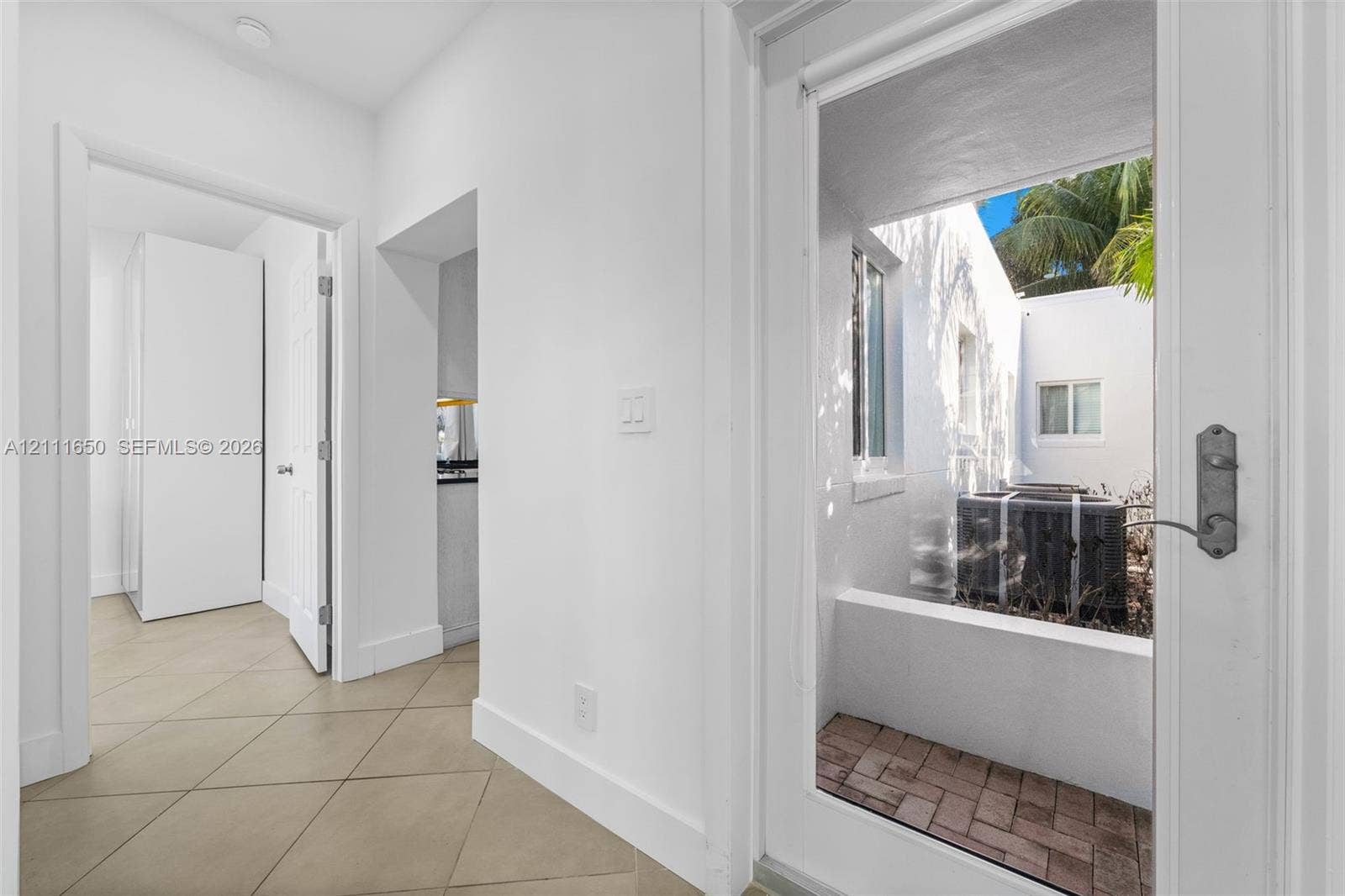 Hallway featuring ceramic tile flooring, solid-core interior doors, and a glass-paneled exterior door opening to a brick-paved patio