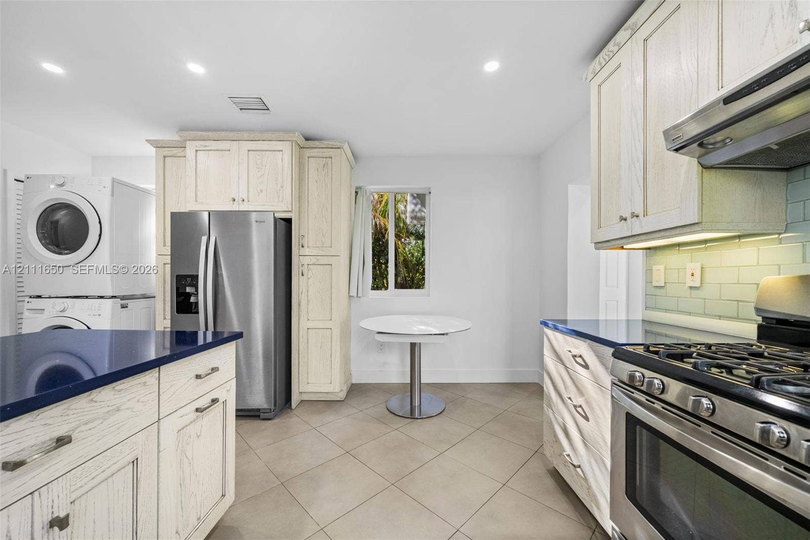 Kitchen featuring light-finish wood cabinetry, dark solid-surface countertops, stainless steel appliances, ceramic tile flooring, and a subway tile backsplash