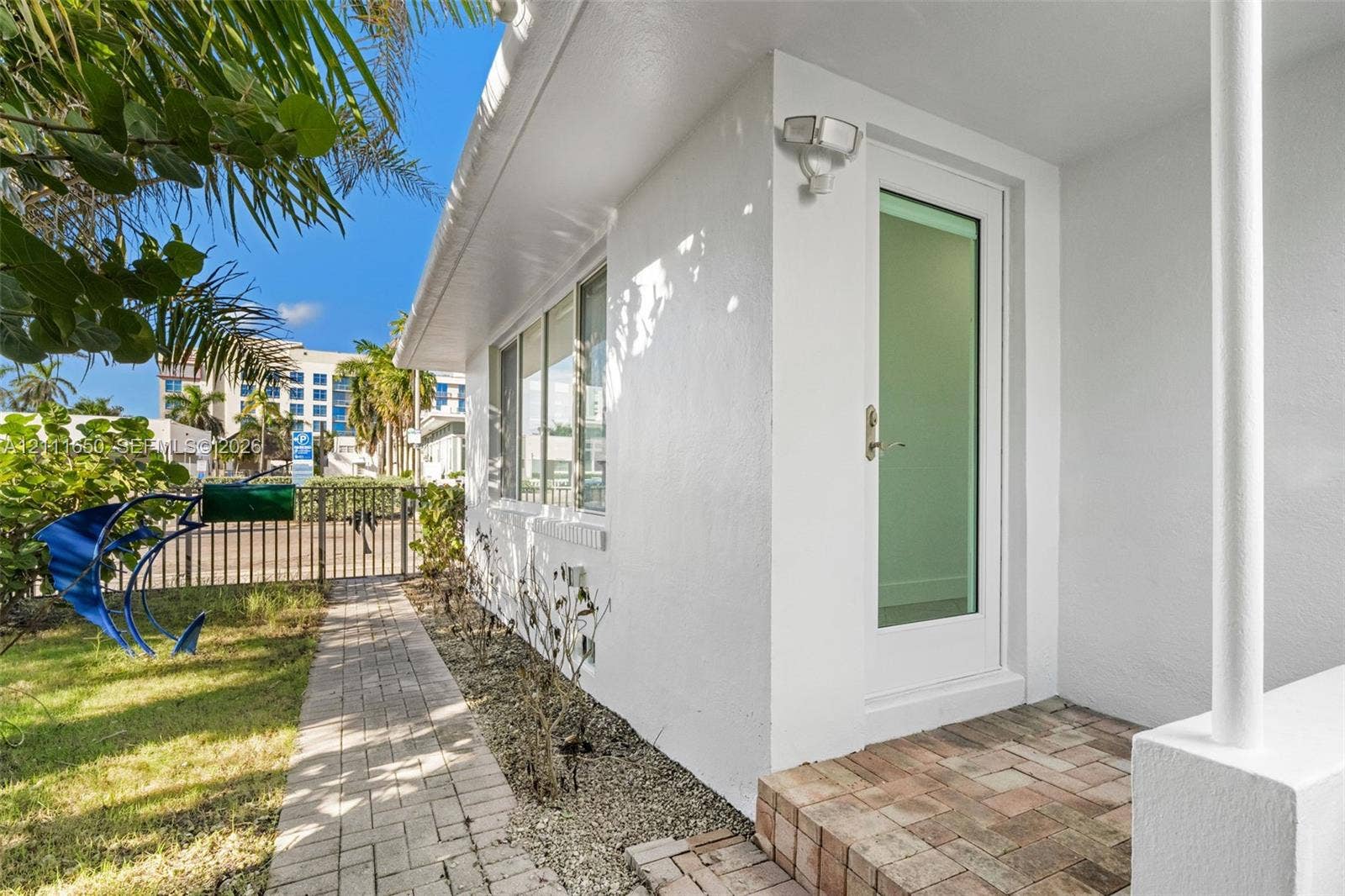 Exterior featuring a white stucco facade, a glass-panel entry door, and a brick paver walkway leading to a brick-paved stoop