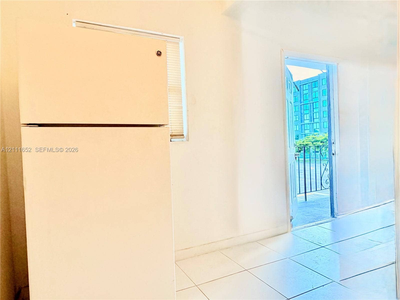 Top-mount refrigerator, neutral tile flooring, and a door providing exterior access to a balcony with metal railings