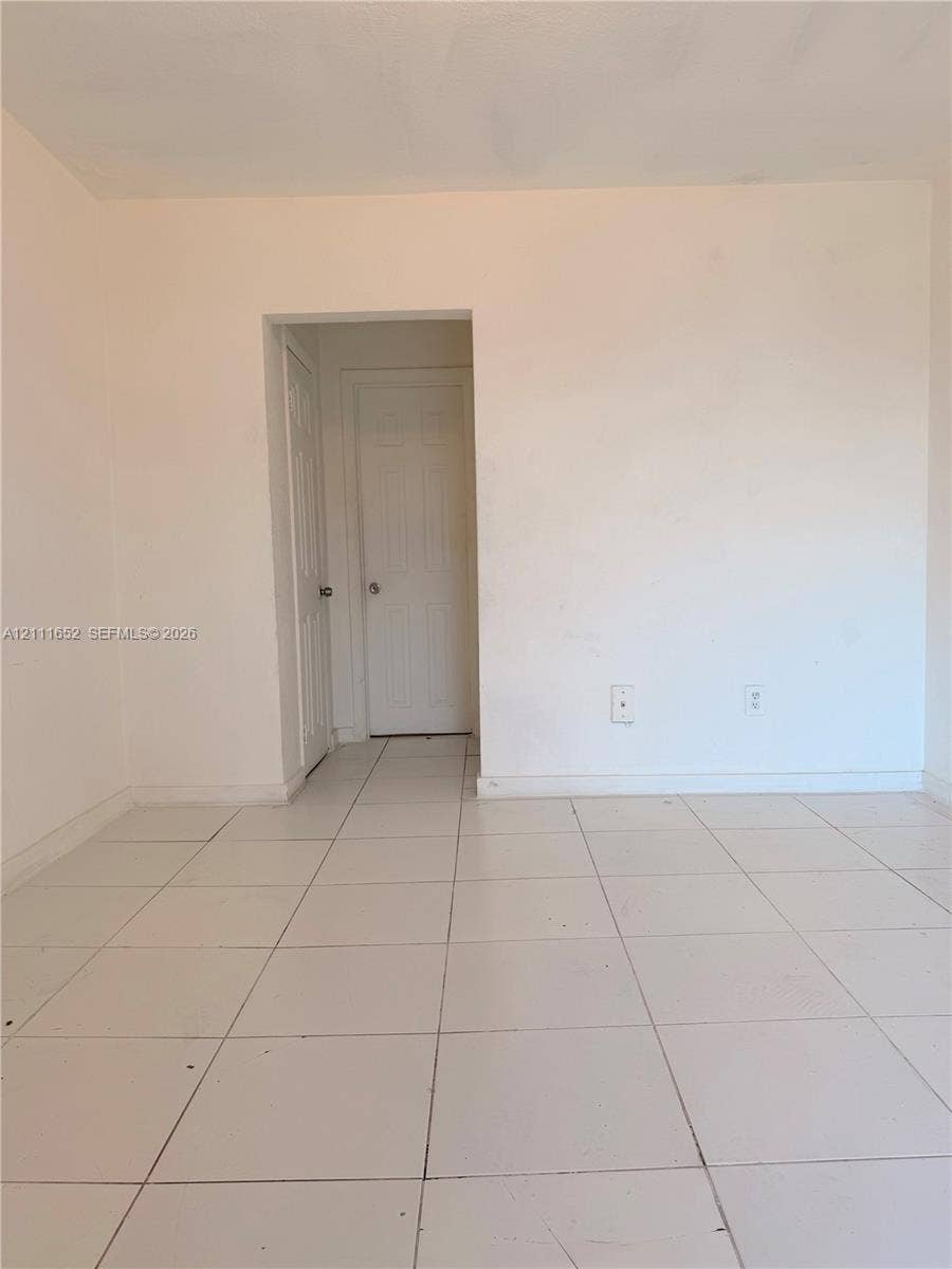Interior space featuring white-painted walls and light-toned square tile flooring with two interior paneled doors