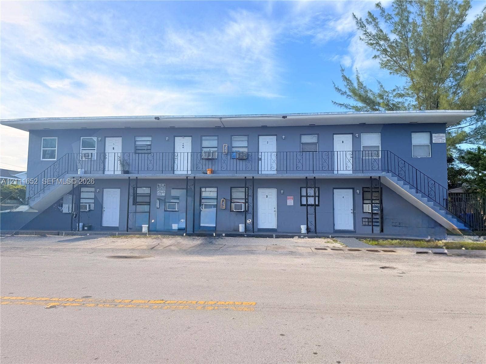 Two-story multi-unit exterior featuring a flat roof, metal railing, and dual exterior staircases