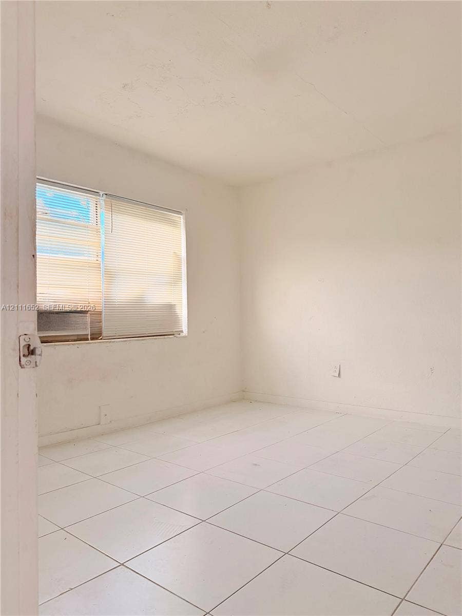 Interior room featuring white tile flooring, neutral wall finishes, and a single-pane sliding window with integrated blinds