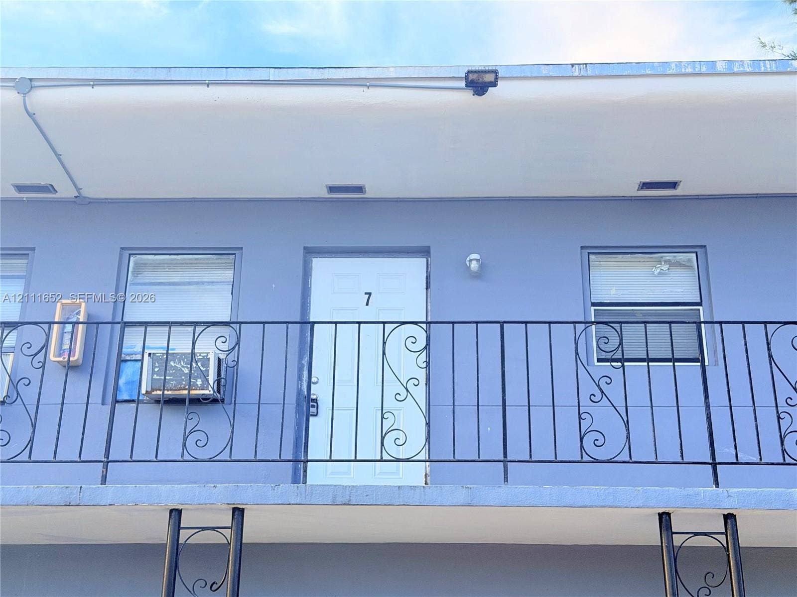 Exterior facade featuring a solid-panel entry door, scroll-work metal balcony railing, and inset windows