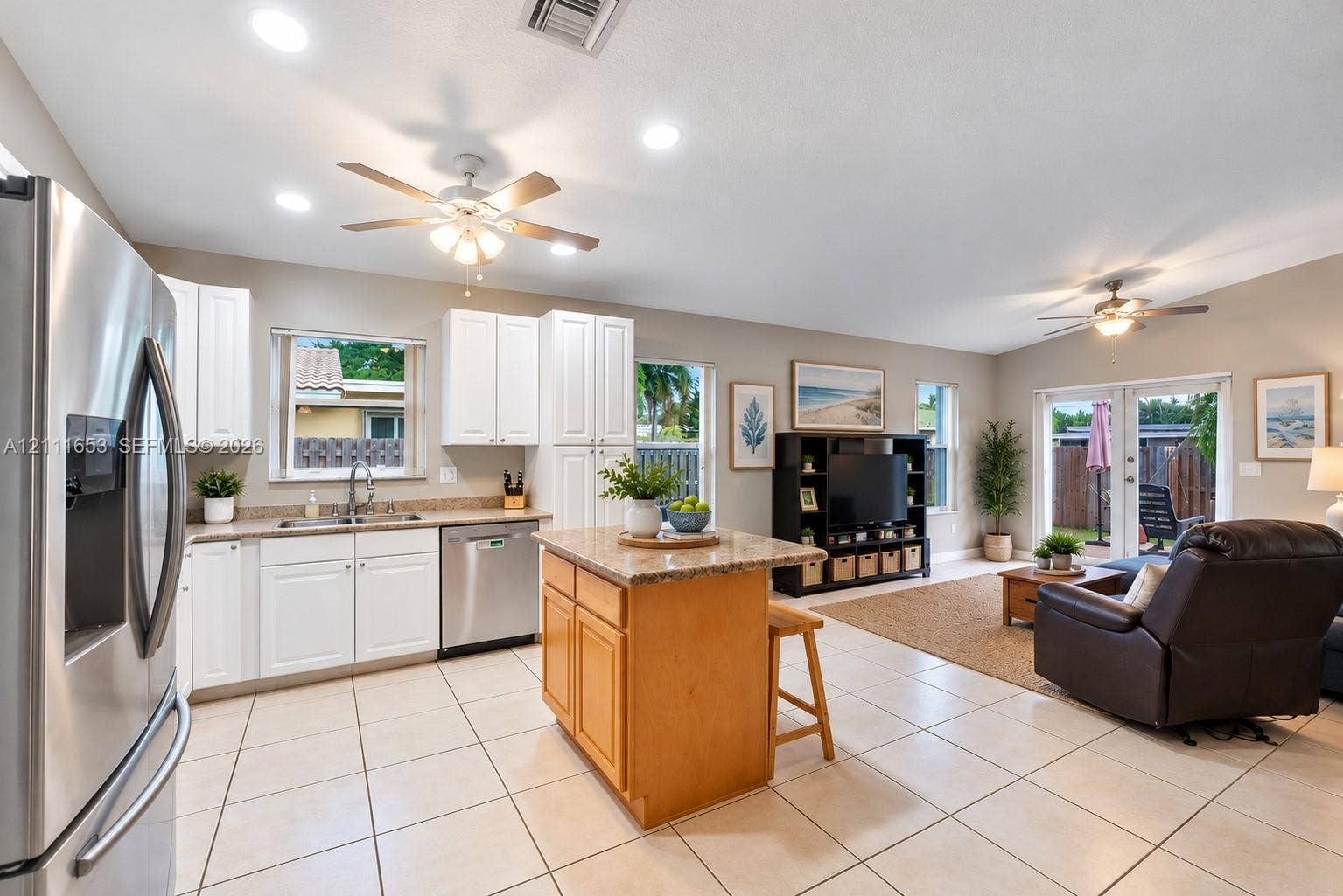 1042 NE 38th Street, Oakland Park, FL 33334 Open-concept kitchen featuring white cabinetry, stone-finish countertops, stainless steel appliances, a center island with wood cabinetry, and neutral-tone tile flooring