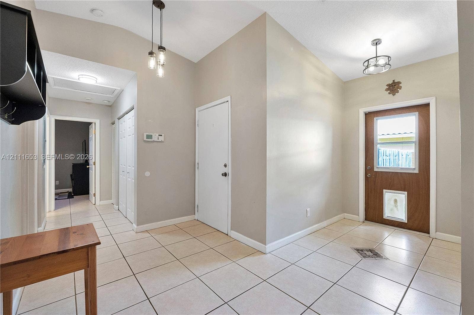 1042 NE 38th Street, Oakland Park, FL 33334 Foyer featuring ceramic tile flooring, vaulted ceilings, multi-light pendant lighting, a glass-panel entry door, and a built-in wall shelf
